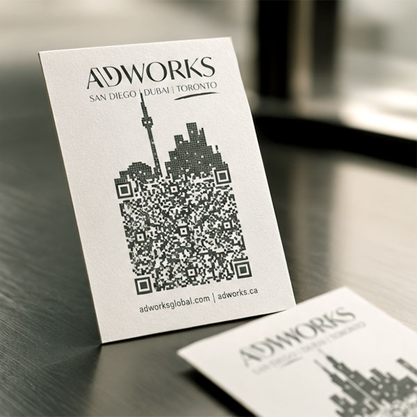 Back of an ADWORKS business card: a city skyline including the CN Tower, drawn entirely from QR-code modules, above adworksglobal.com and adworks.ca