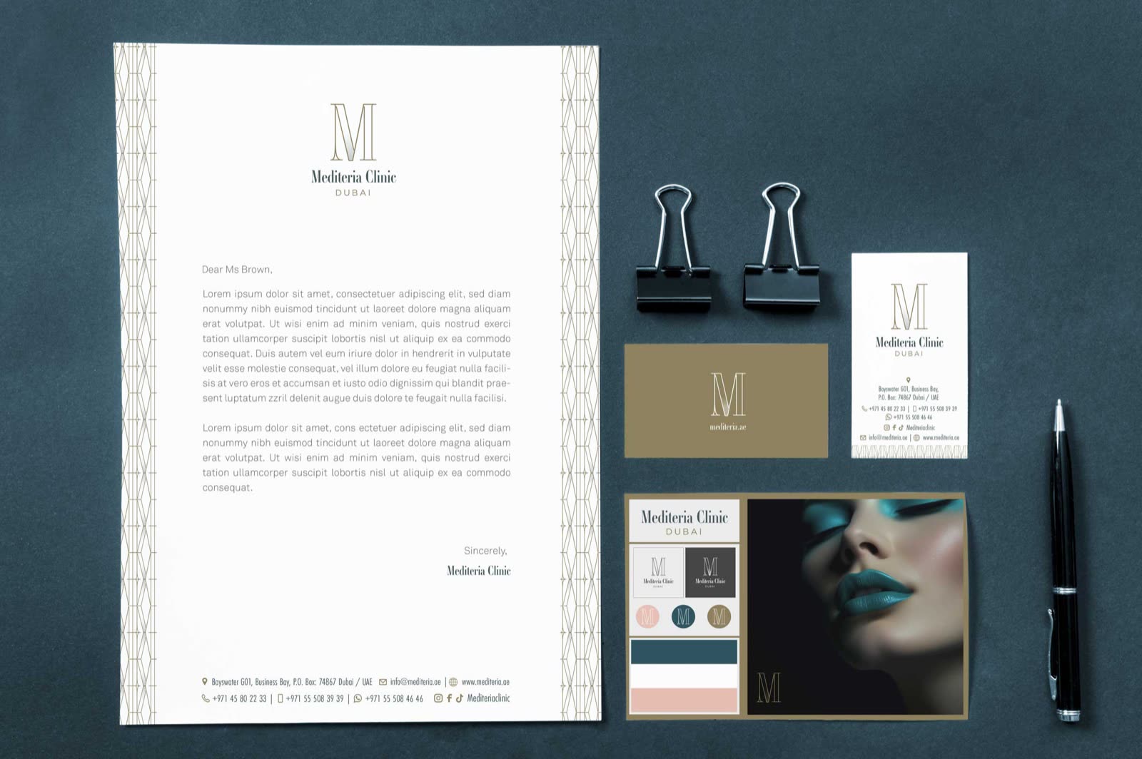 Mediteria stationery on a dark teal surface: letterhead, cards and envelopes with the gold M